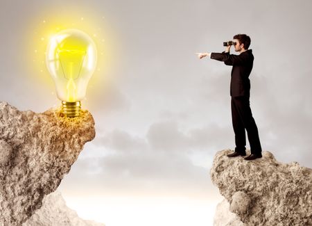 Businessman standing on the edge of mountain with an idea bulb on the other side 