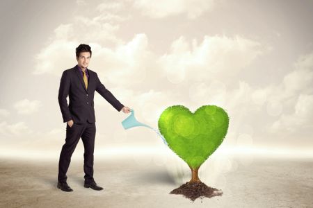 Business man watering heart shaped green tree concept on background