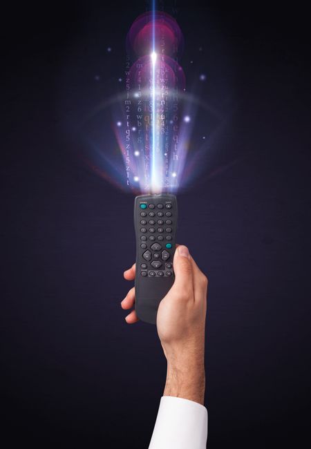Hand holding a remote control, shining numbers and letters coming out of it 
