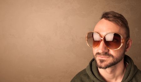 Portrait of a young pretty man with sunglasses and copyspace on brown background