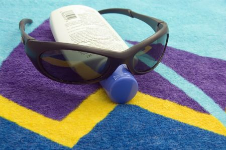 Sunglasses and bottle of sunscreen on beach towel