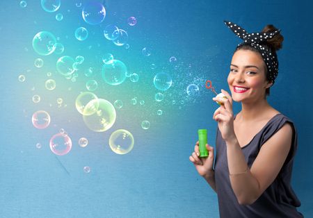 Pretty lady blowing big colorful bubbles on blue background