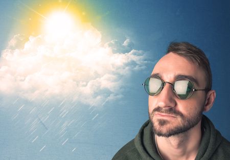 Young person looking with sunglasses at clouds and sun concept on blue background