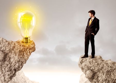 Businessman standing on the edge of mountain with an idea bulb on the other side 