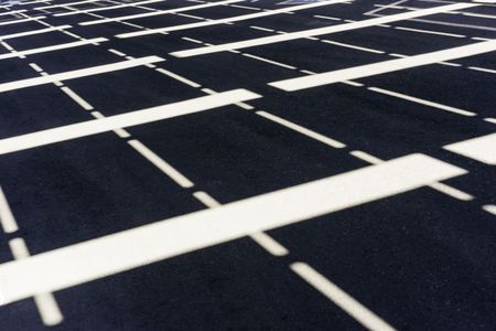 Symmetrical pattern of sunlight and white stripes on asphalt parking lot