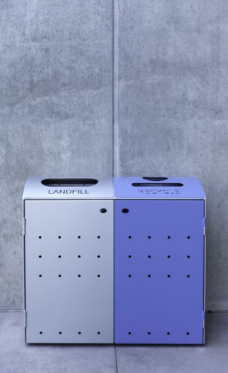 Landfill and recycle bins, one silver one blue, by exterior gray concrete wall on university campus