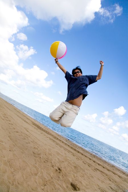 beach guy jumping of joy with ball on a sunny day with a blue sky in the background
