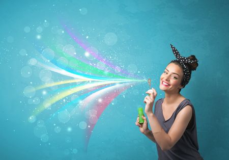Beautiful girl blowing abstract colorful bubbles and lines on blue background