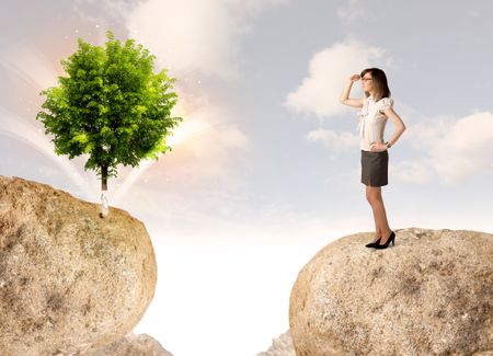 Businesswoman standing on the edge of rock mountain with a tree on the other side 