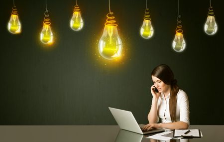 Businesswoman sitting at the black table with idea bulbs on the background 