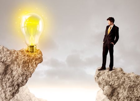 Businessman standing on the edge of mountain with an idea bulb on the other side