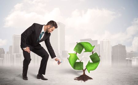 Business man watering green recycle sign tree on city background concept