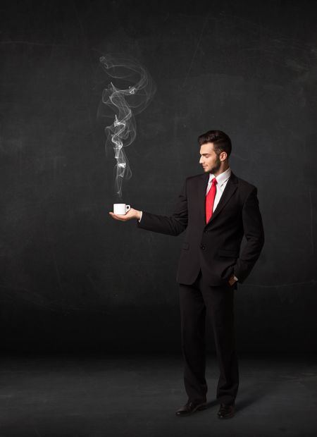 Businessman standing and holding a white steamy cup on a black background

