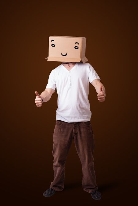 Young man standing and gesturing with a cardboard box on his head with smiley face