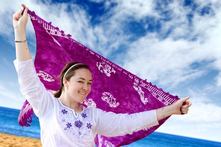 beautiful girl having fun at the beach waving a purple sarong