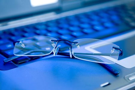business glasses on a laptop keyboard in blue tones