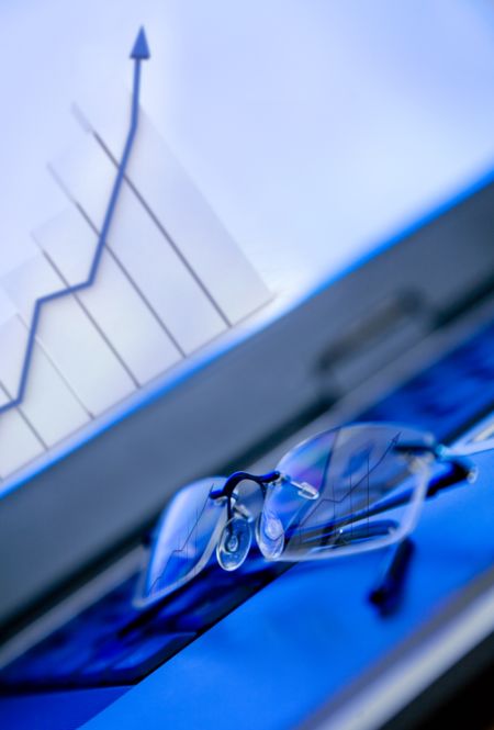 glasses on laptop showing a growth financial graph on the screen - focus is on the graph reflection on the glasses