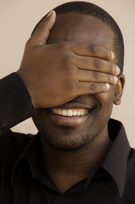 Grinning young black man hiding his eyes with his right hand