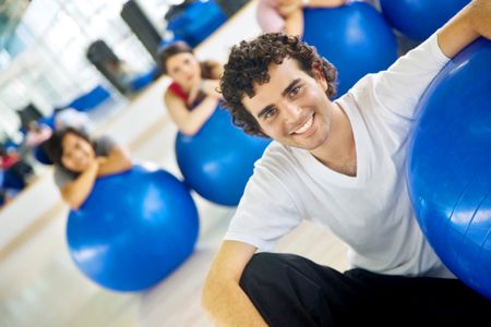 Gym man portrait leaning on a pilates ball in front of a group