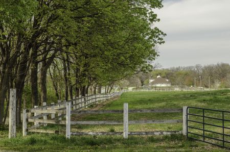 Haven for retired horses: Shaded paddock, enclosed by long weathered fence with iron gate, at a public equestrian center in spring, northern Illinois