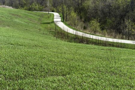 Spring beckons: Bright trail of crushed limestone curves out of sight between grassy hillside and deciduous woods in Meacham Grove Forest Preserve in northern Illinois on a sunny afternoon in April