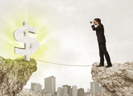 Businessman standing on the edge of mountain with a shining dollar mark on the other side