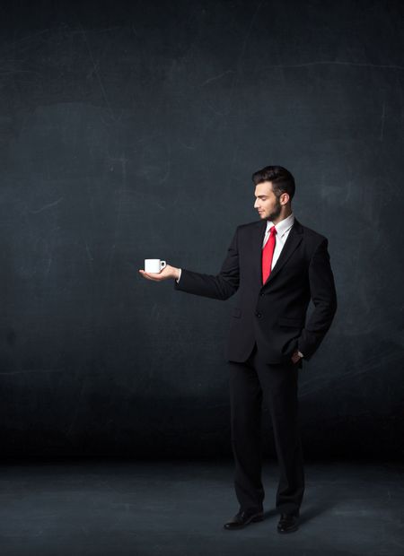 Businessman standing and holding a white cup on a black background

