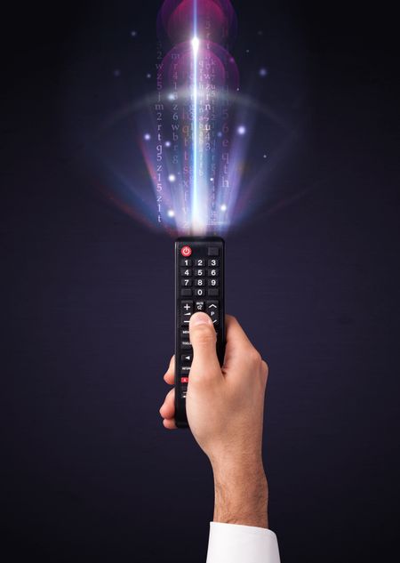 Hand holding a remote control, shining numbers and letters coming out of it
