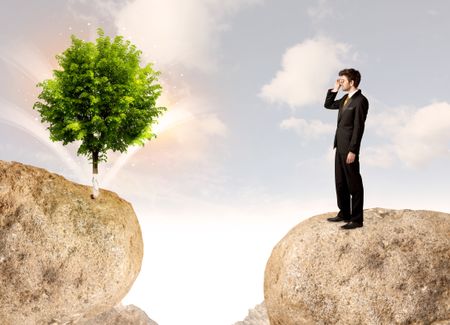 Businessman standing on the edge of rock mountain with a tree on the other side
