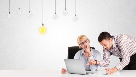 Business man and woman sitting at table with bright idea light bulbs