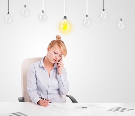 Business woman sitting at table with bright idea light bulbs