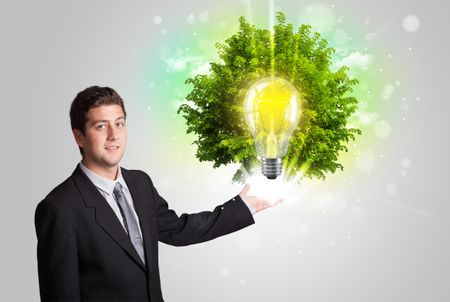 Young man presenting idea light bulb with green tree concept