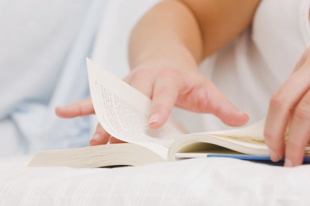 Close up of a girl reading a book on her bed.