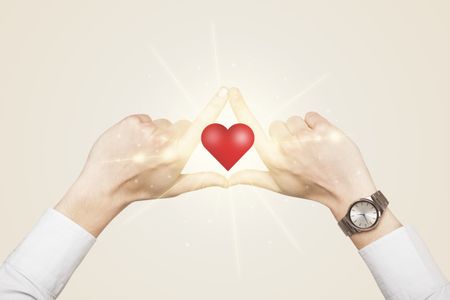 Hands creating a form with shining red heart in the center