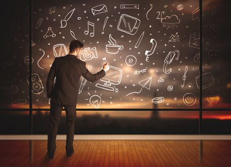 Businessman drawing media icons on glass window, bokeh cityscape background
