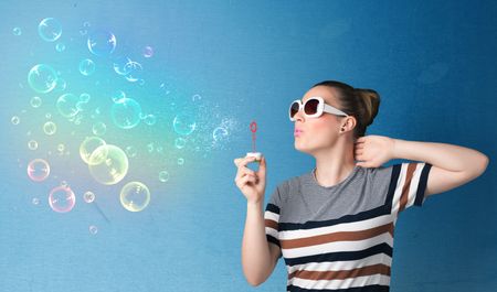 Pretty lady blowing big colorful bubbles on blue background