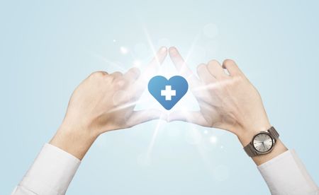 Hands creating a form with shining heart blue cross in the center