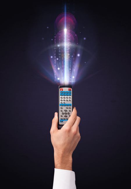 Hand holding a remote control, shining numbers and letters coming out of it
