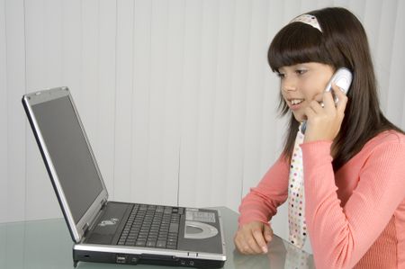 Girl in pink talking on cell phone and smiling at computer monitor