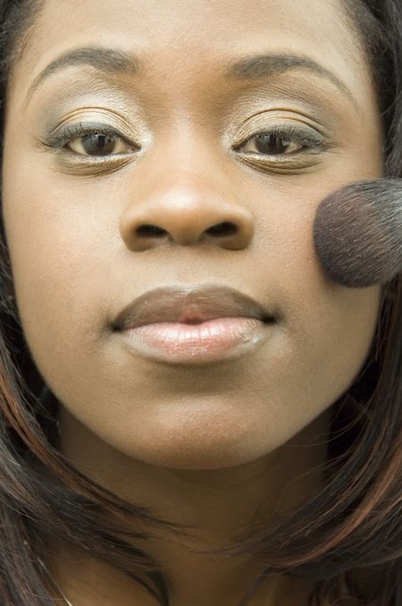 Close-up of young black woman applying cosmetic brush to her left cheek