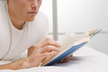 Close up of a guy reading a book on the bed.