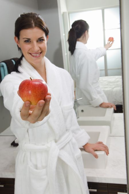 Attractive woman holding an apple in bathroom.