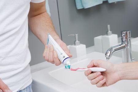 Guy putting toothpaste on girlfriends toothbrush.