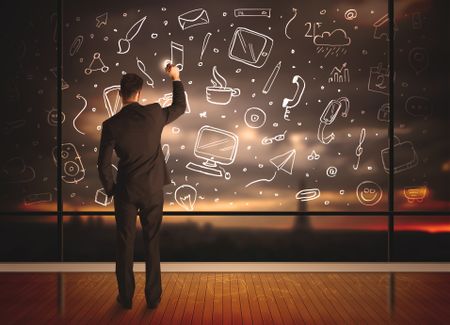 Businessman drawing media icons on glass window, bokeh cityscape background
