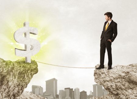 Businessman standing on the edge of mountain with a shining dollar mark on the other side