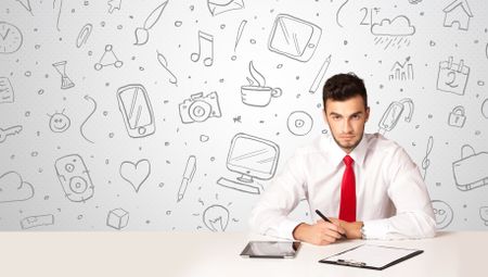 Businessman sitting at table with hand drawn media icons and symbols 