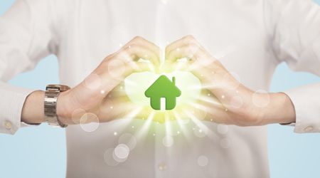 Hands creating a form with shining green house in the center
