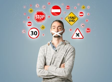 Young man with taped mouth and traffic signals around his head  