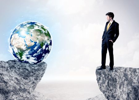 Businessman standing on the edge of mountain with a globe on the other side
