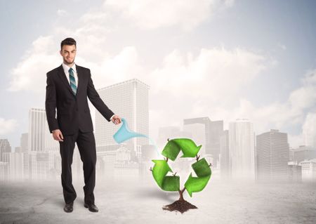 Business man watering green recycle sign tree on city background concept